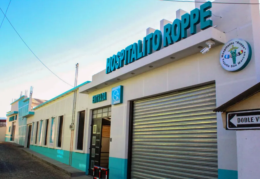 Fachada del Hospitalito Roppe, edificio blanco con franjas turquesa y el nombre del hospital en la pared